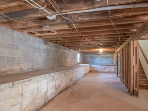 An unfinished basement with concrete block walls, wood joists and a concrete floor