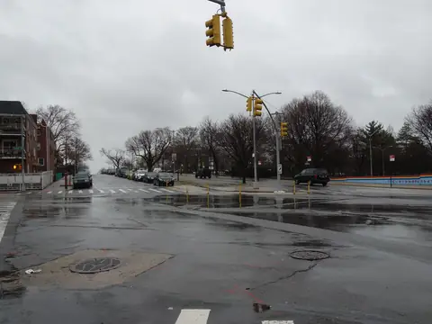 A wide Corona intersection on a rainy day, with wet pavement and apartment buildings