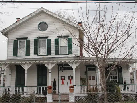An older white frame house with a deep front porch in Corona, Queens