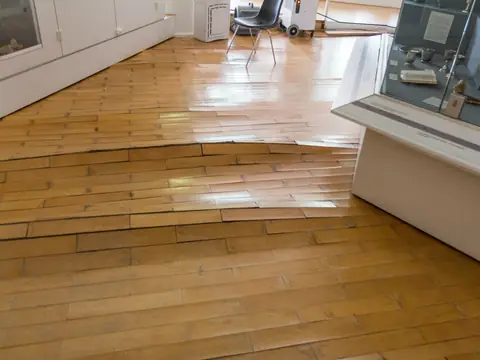 Wood floorboards buckled by water, with a dehumidifier running in the background
