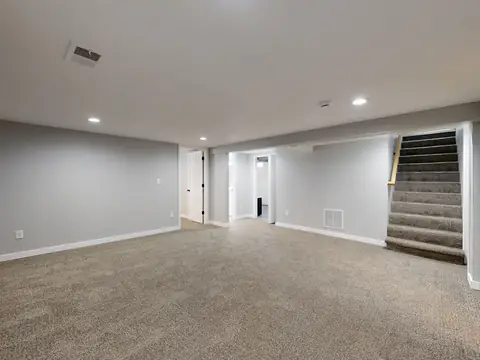 A finished basement with carpet, recessed lights and a staircase
