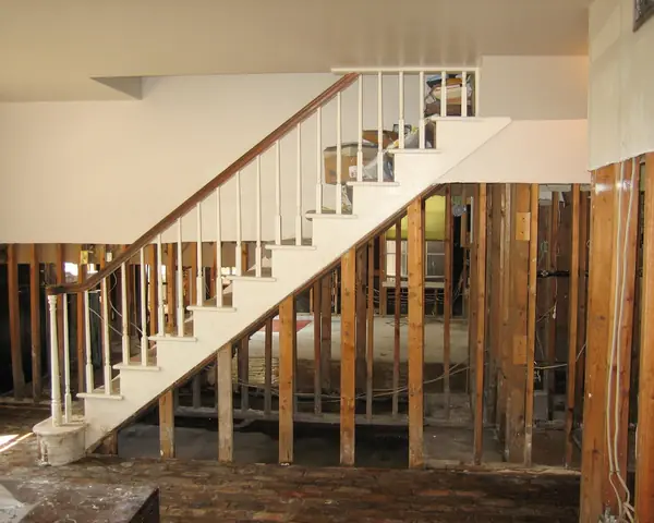 Inside a flood-damaged house: the walls opened to the studs below the water line around a white staircase