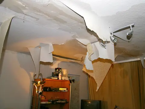 A ceiling torn open with drywall paper hanging down after water came through from above
