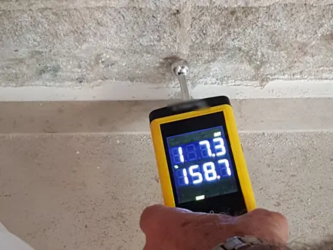 A moisture meter pressed against a concrete block wall