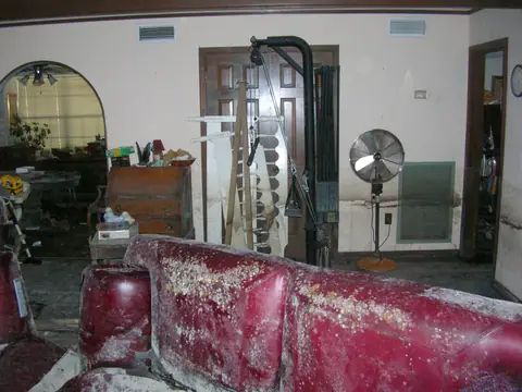 Mold on the walls and furniture of a flooded living room, with a standing fan
