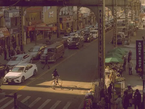 Shops and traffic along an avenue under an elevated train line in Queens