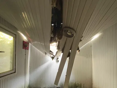 A collapsed ceiling hanging open over a debris-covered floor