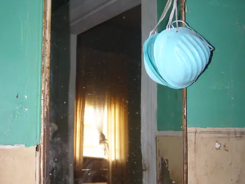 A dust mask hanging in the doorway of a gutted, water-damaged room