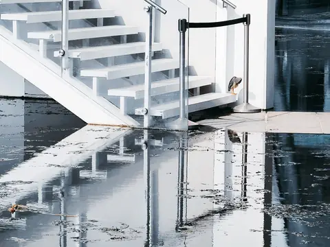 Water covering a concrete floor at the foot of a white staircase