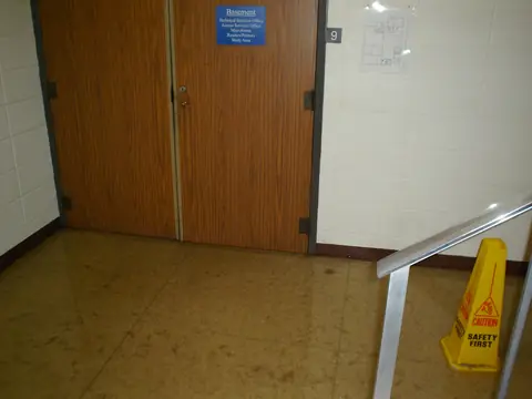 Water spread across a floor outside a pair of basement doors, with a caution sign by the stairs