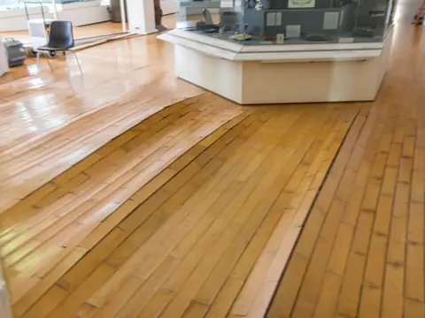 Wood floorboards lifted and buckled by water in a bright room