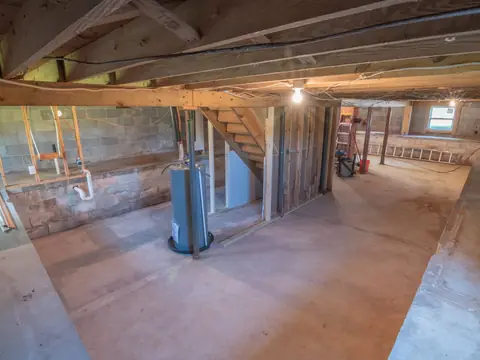 An unfinished basement with a water heater, wood framing and a bare concrete floor