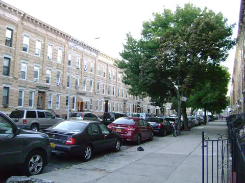 A Ridgewood street lined with attached three-story brick buildings and street trees
