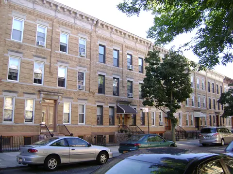 A row of attached yellow-brick buildings with stoops and awnings in Ridgewood, Queens