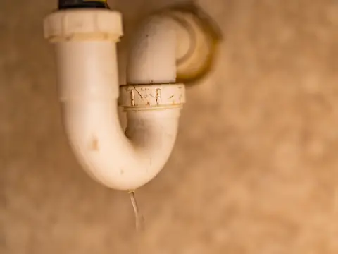 A white plastic drain pipe under a sink with water dripping from its joint