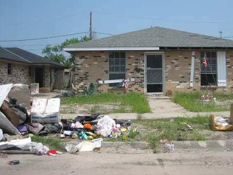 Ruined furniture and belongings piled at the curb in front of a brick house after a flood