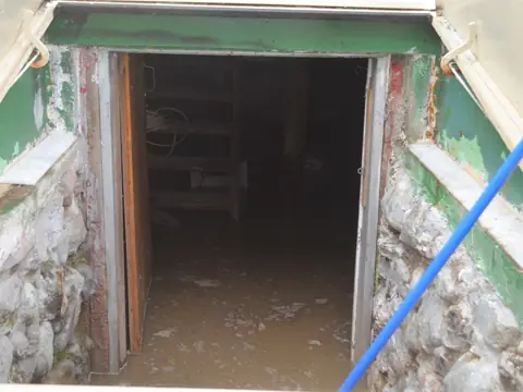 Muddy floodwater standing inside an open cellar doorway in a stone foundation