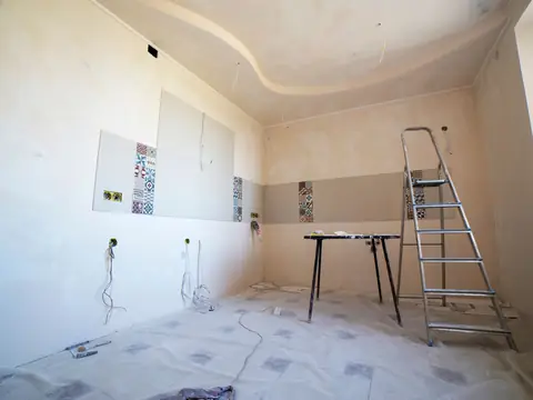 A bright room part way through repairs, with new drywall, a ladder and a covered floor