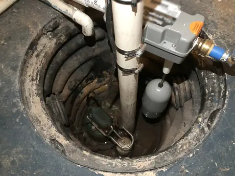 A sump pump sitting in its pit in a basement floor