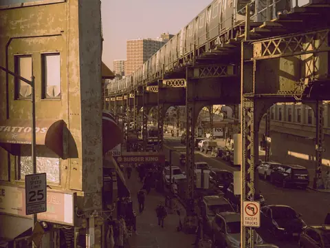 An elevated train passing over a street of shops and parked cars